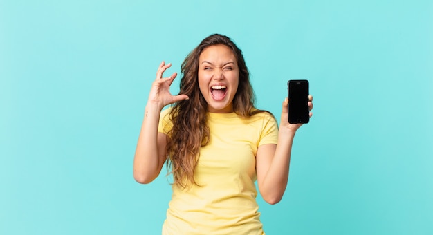 Jeune jolie femme criant avec les mains en l'air et tenant un téléphone intelligent