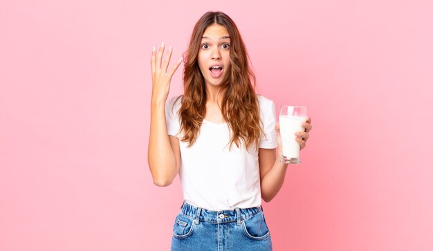 Jeune jolie femme criant avec les mains en l'air et tenant un verre de lait