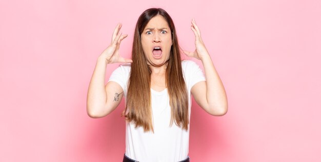 Jeune jolie femme crier avec les mains en l'air, se sentir furieuse, frustrée, stressée et bouleversée