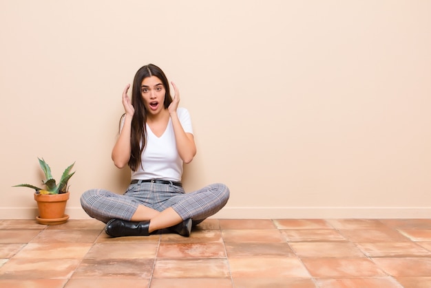 Jeune jolie femme crier avec les mains en l'air, se sentir furieux, frustré, stressé et bouleversé assis sur un sol