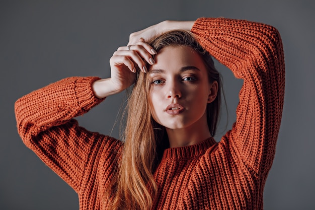 Jeune jolie femme dans un pull rouge sur fond gris