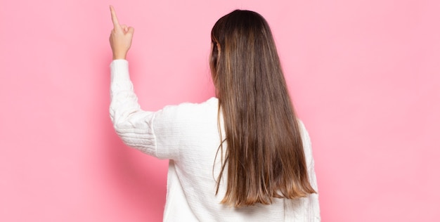 Jeune jolie femme debout et pointant vers l'objet sur l'espace de copie, vue arrière