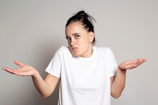 Jeune jolie femme est surprise et perplexe lève les mains dans la confusion et hausse les épaules