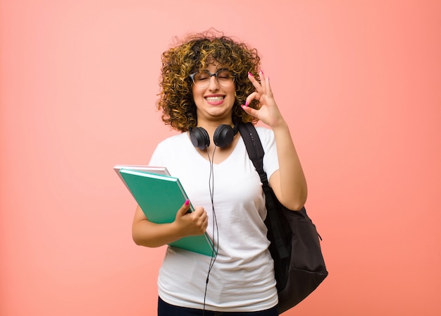 Jeune jolie femme étudiante à la concentration et à la méditation, se sentant satisfaite et détendue, pensant ou faisant un choix contre le mur rose