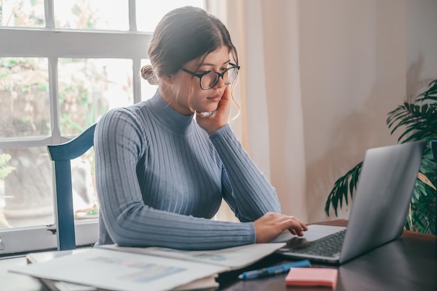 Une jeune jolie femme étudie et fait ses devoirs à la maison sur la table Adolescente utilisant un ordinateur portable ou un ordinateur surfant sur le net à l'intérieur