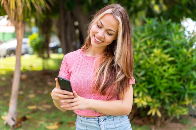 Jeune jolie femme à l'extérieur à l'aide d'un téléphone portable avec une expression heureuse