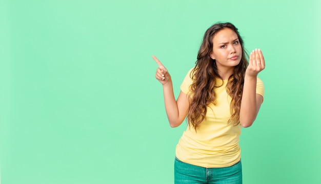 Jeune jolie femme faisant un geste de capice ou d'argent, vous disant de payer et pointant vers l'espace de copie