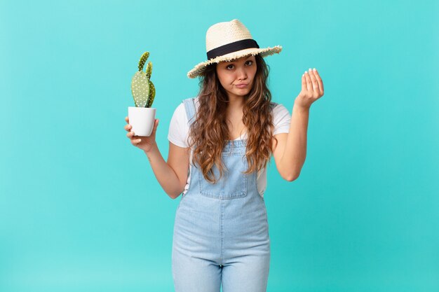 Jeune jolie femme faisant un geste de capice ou d'argent, vous disant de payer et tenant un cactus