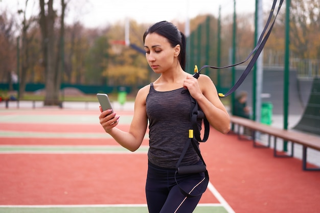 Jeune jolie femme fait une formation de suspension avec des sangles de fitness en plein air