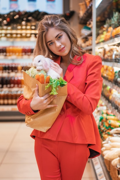 La jeune jolie femme fait ses courses pour acheter des légumes pour son lapin blanc au supermarché