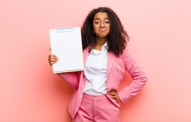 Jeune jolie femme avec une feuille de papier contre le mur rose