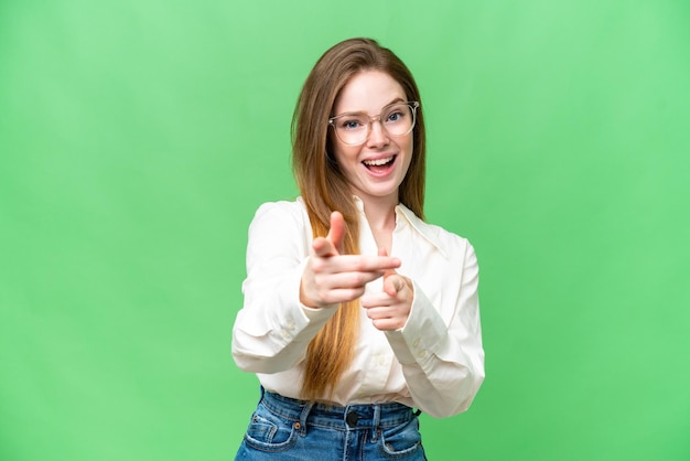 Jeune jolie femme sur fond isolé chroma key surpris et pointant vers l'avant