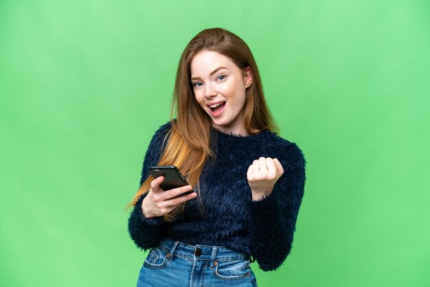 Jeune jolie femme sur fond isolé chroma key avec téléphone en position de victoire