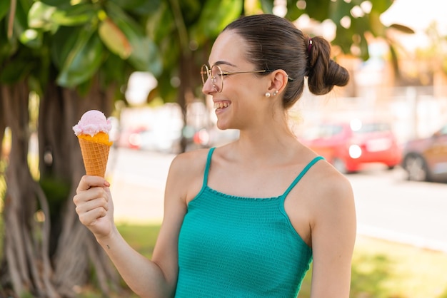 Jeune jolie femme avec une glace au cornet à l'extérieur avec une expression heureuse