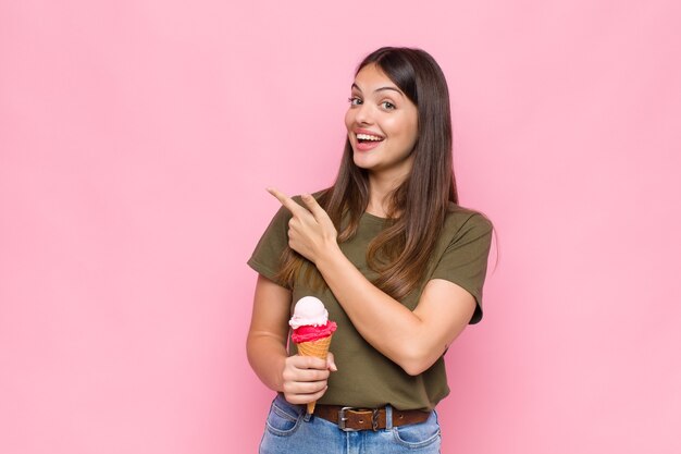 Jeune jolie femme avec une glace à excité et surpris en pointant vers le côté et vers le haut pour copier l'espace