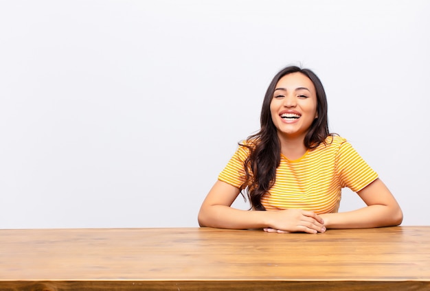 Jeune jolie femme avec un grand sourire amical et insouciant, l'air positif, détendu et heureux, se détendre contre le mur plat