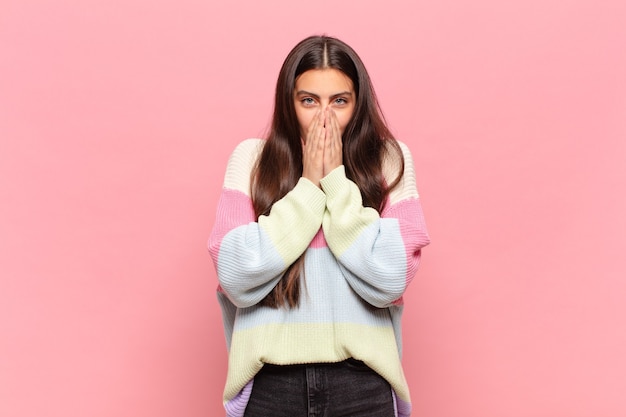 Jeune jolie femme heureuse et excitée, surprise et étonnée couvrant la bouche avec les mains, riant avec une expression mignonne