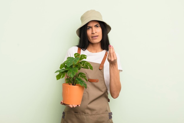 Jeune jolie femme hispanique faisant un capice ou un geste d'argent vous disant de payer le concept d'agriculteur ou de jardinier