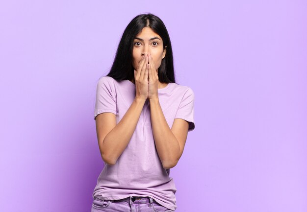 Jeune jolie femme hispanique heureuse et excitée, surprise et étonnée couvrant la bouche avec les mains, riant avec une expression mignonne