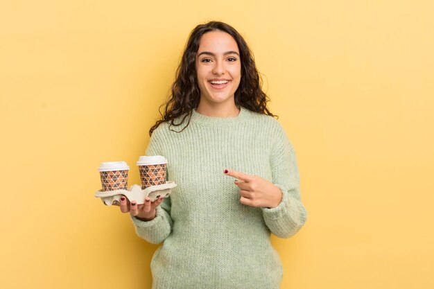 jeune jolie femme hispanique qui a l'air excitée et surprise en pointant sur le côté. concept de café à emporter