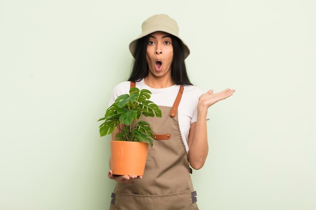 Jeune jolie femme hispanique qui a l'air surprise et choquée par la chute de la mâchoire tenant un concept d'agriculteur ou de jardinier d'objet