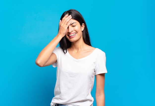 Jeune jolie femme hispanique riant et frappant le front comme disant d'oh ! J'ai oublié ou c'était une erreur stupide