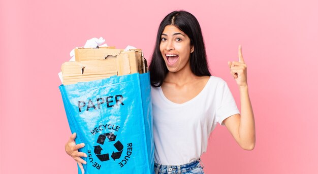 Jeune jolie femme hispanique se sentant comme un génie heureux et excité après avoir réalisé une idée et tenant un sac en papier à recycler