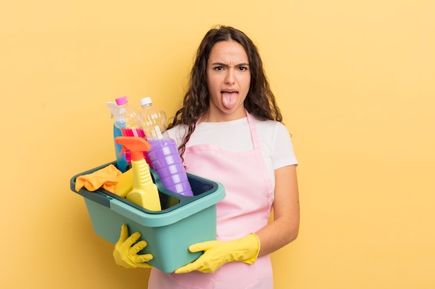 Jeune jolie femme hispanique se sentant dégoûtée et irritée et tirant la langue des travaux ménagers un concept de produits propres