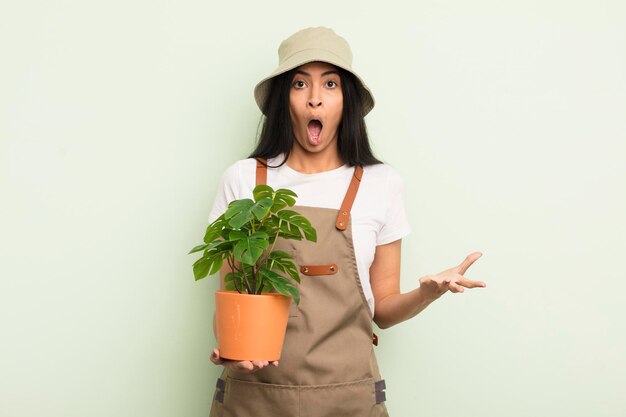 Jeune jolie femme hispanique se sentant extrêmement choquée et surprise du concept d'agriculteur ou de jardinier