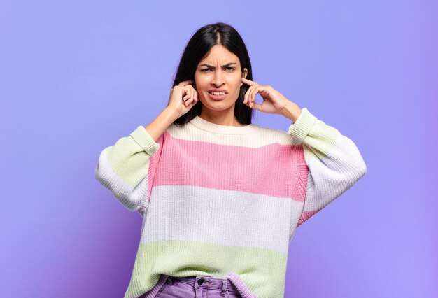 Jeune jolie femme hispanique semblant en colère, stressée et agacée, couvrant les deux oreilles à un bruit assourdissant, un son ou une musique forte