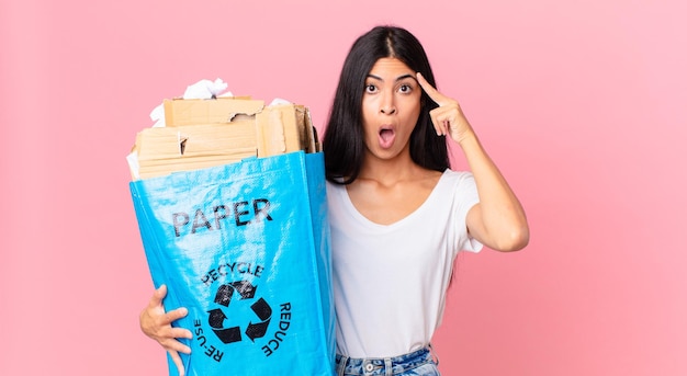 Jeune jolie femme hispanique semblant surprise, réalisant une nouvelle pensée, idée ou concept et tenant un sac en papier à recycler