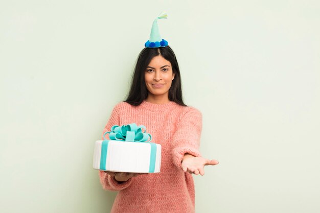 Jeune jolie femme hispanique souriant joyeusement avec amical et offrant et montrant un concept de concept de gâteau d'anniversaire