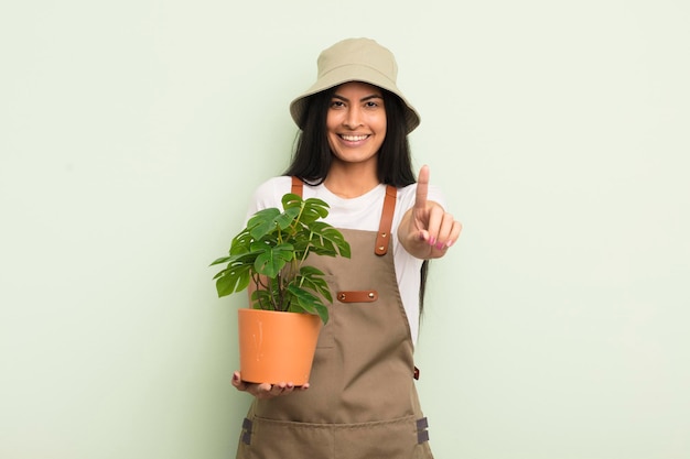 Jeune jolie femme hispanique souriante et amicale montrant le concept d'agriculteur ou de jardinier numéro un