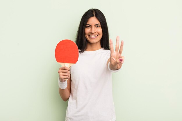 Jeune jolie femme hispanique souriante et amicale montrant le concept de ping-pong numéro trois