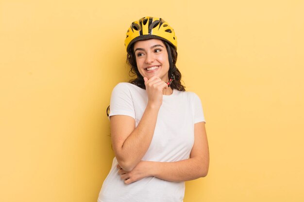 Jeune jolie femme hispanique souriante avec une expression confiante heureuse avec la main sur le concept de vélo de menton