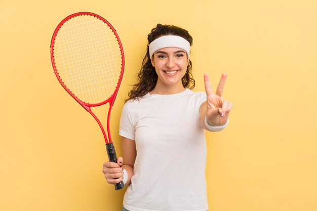 Jeune jolie femme hispanique souriante et regardant heureuse gesticulant victoire ou concept de tennis de paix
