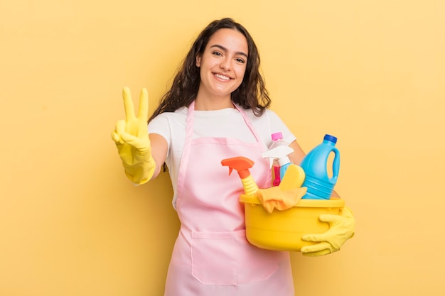 Jeune jolie femme hispanique souriante et sympathique montrant le numéro deux des travaux ménagers un concept de produits propres