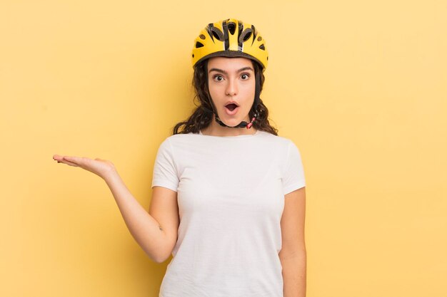 Jeune jolie femme hispanique à la surprise et choquée avec la mâchoire tombée tenant un concept de vélo d'objet