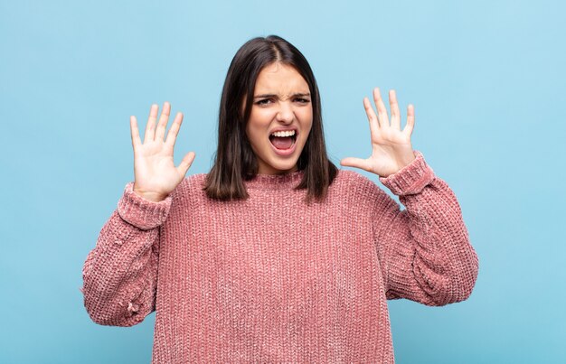 Jeune jolie femme hurlant de panique ou de colère, choquée, terrifiée ou furieuse, avec les mains à côté de la tête