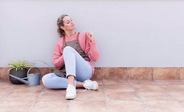 Jeune jolie femme jardinière blonde assise sur le sol avec un espace de copie sur le côté