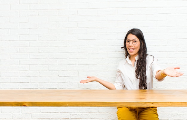 Jeune jolie femme latine à l'air heureuse, arrogante, fière et satisfaite, se sentir comme une numéro un assise devant une table