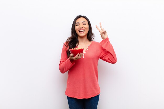 Jeune jolie femme latine contre un mur plat avec un bol de petit déjeuner