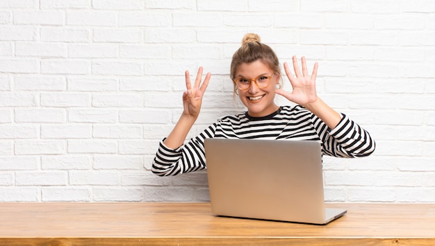 Jeune jolie femme latine, souriant et sympathique, montrant le numéro huit ou huitième avec la main vers l'avant, compte à rebours assis avec son ordinateur portable