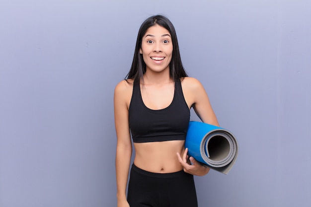 Jeune jolie femme latine avec un tapis de yoga contre le mur de ciment