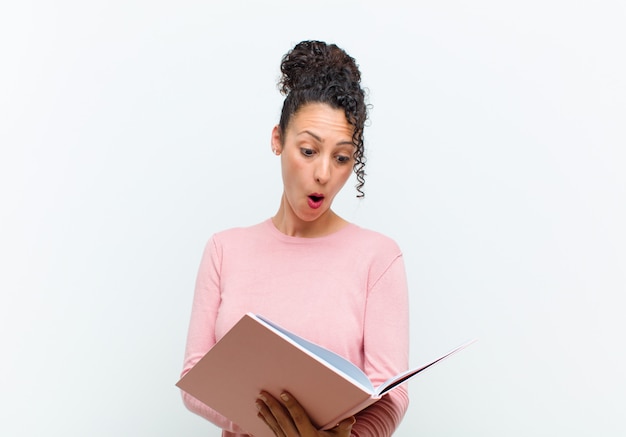 Jeune jolie femme avec des livres contre un mur blanc