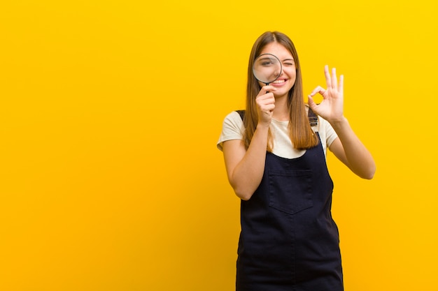 Jeune jolie femme avec une loupe contre orange