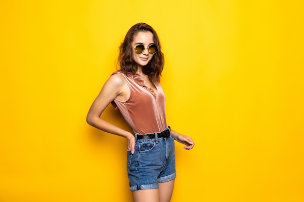 Jeune jolie femme avec des lunettes de soleil sur un jaune