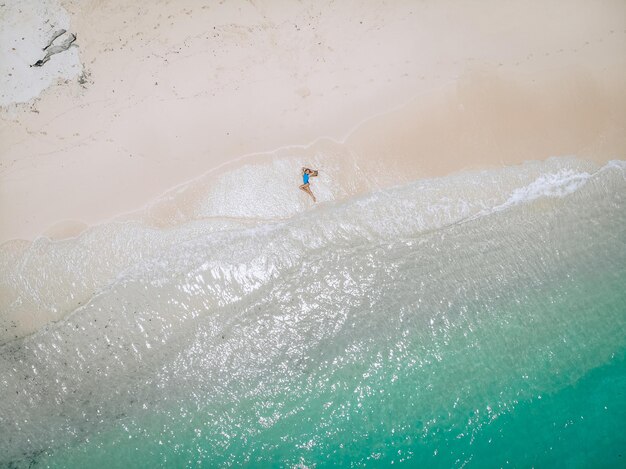 Jeune jolie femme en maillot de bain bleu allongé sur une plage de sable pendant la marée. Concept de vacances d'été