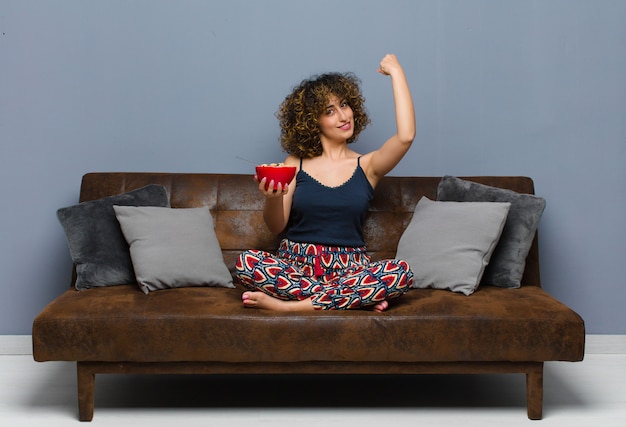 Photo jeune jolie femme à la maison assise sur un canapé et prenant un petit déjeuner