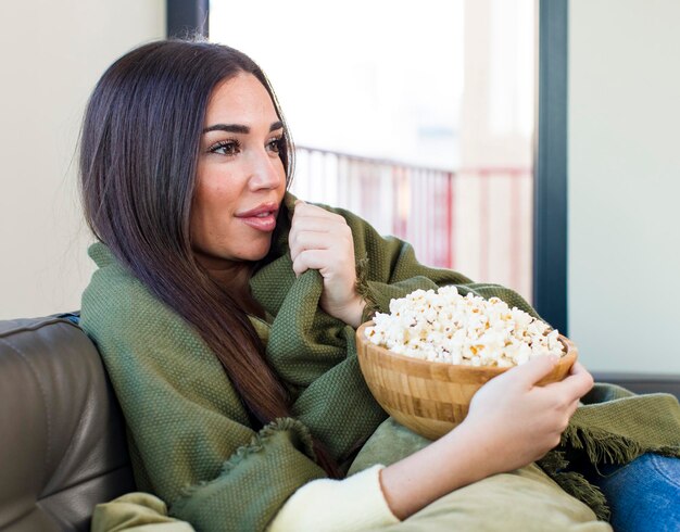 Jeune jolie femme mangeant des pop-corn assis sur un canapé à la maison